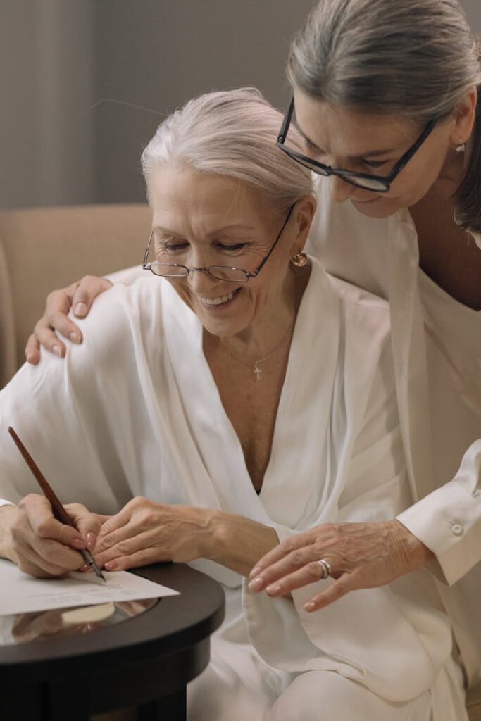 Two senior women sharing a moment of joy and togetherness while writing indoors.