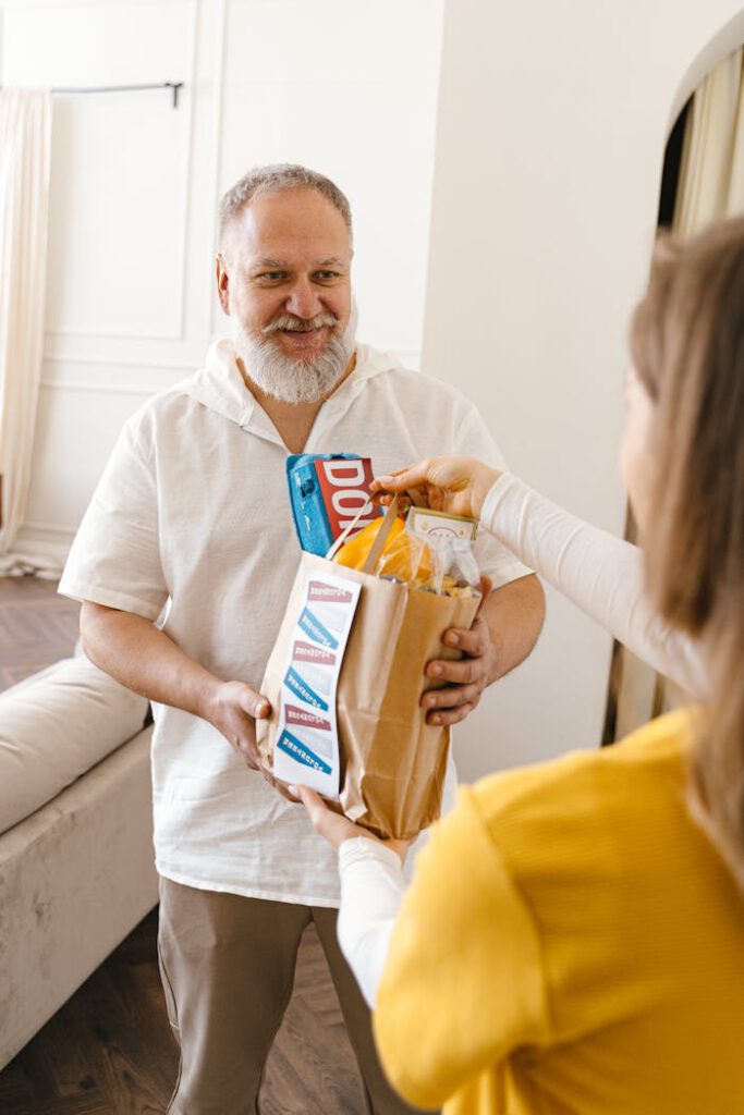 Elderly man receives food donation inside a warm and inviting home setting.