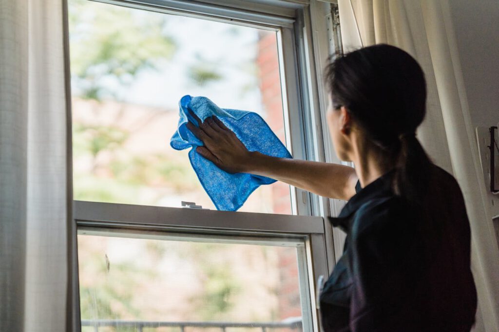 A woman cleans a window using a blue microfiber cloth providing a streak-free shine.